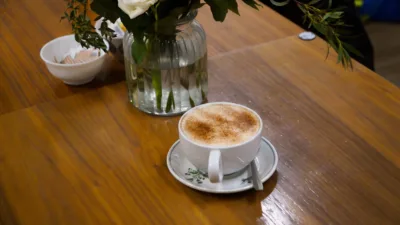 a cup of coffee by a vase of flowers on a table